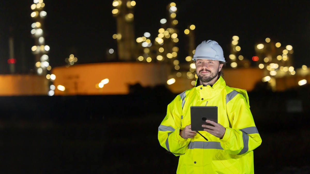 Trabajador de la industria energética con tablet frente a instalaciones industriales de noche