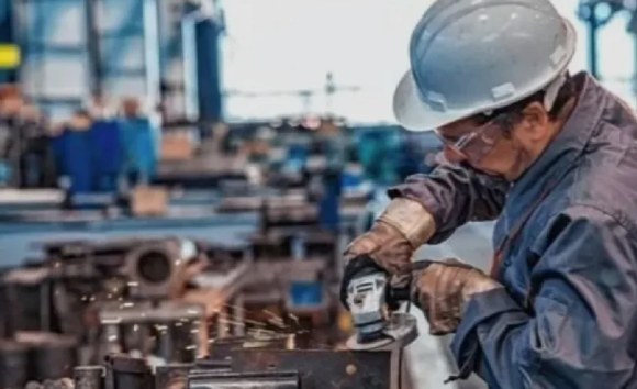 Operario con casco y anteojos de seguridad trabajando con una amoladora en un taller metalúrgico