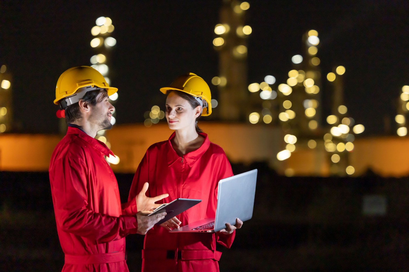 Trabajadores de la industria energética con equipos frente a instalaciones industriales iluminadas de noche